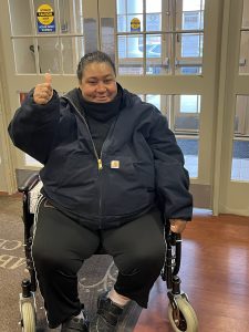 Woman sitting in a wheelchair giving a thumbs up and smiling. 